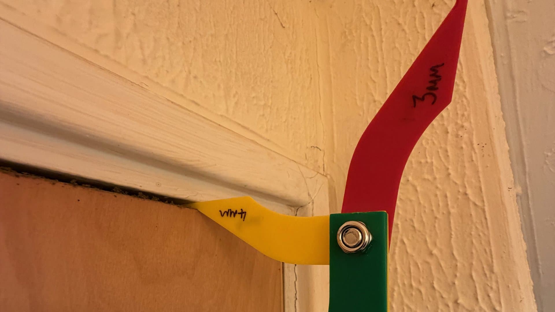 Stepped gap gauge showing 3 mm and 4 mm blades at the head and jamb of a fire door