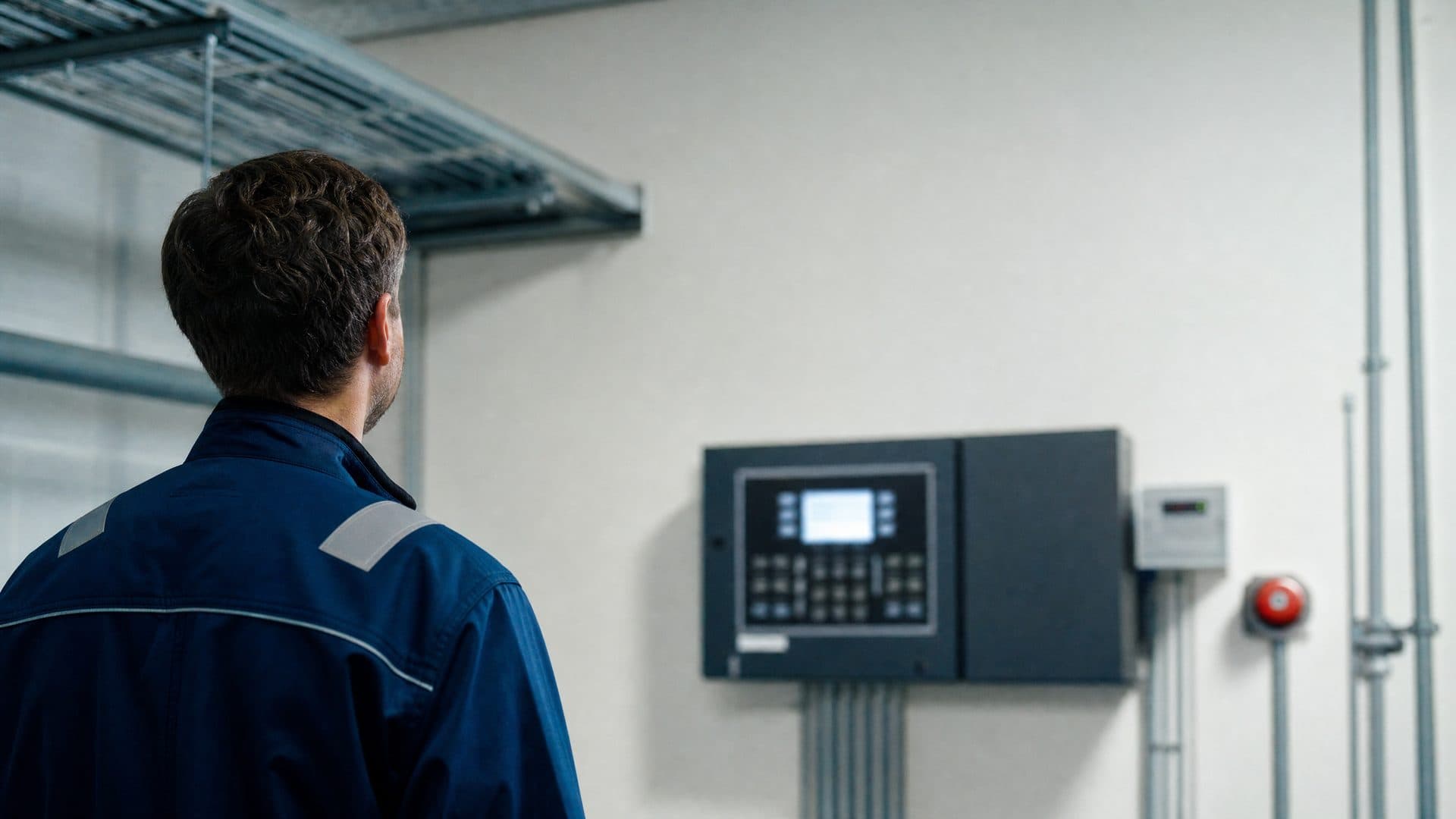 Illustrative: an engineer from behind at a fire alarm control panel